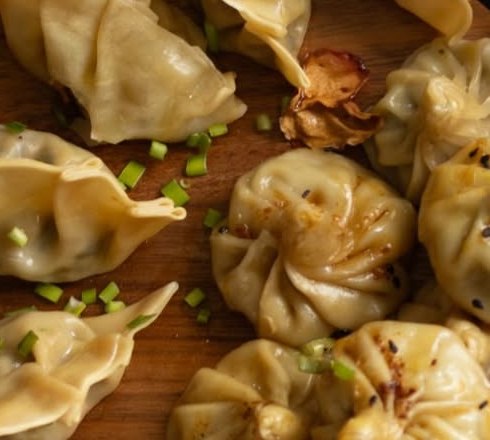 Gyozas y momos sobre una tabla de madera con cebollín